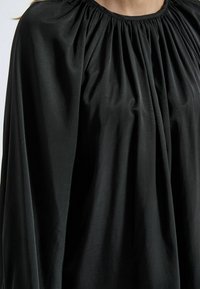 Schwarze, fließende Bluse mit gerafftetem Halsausschnitt, die eine glatte Textur und lockere Passform bietet. Der weiche Stoff fällt elegant über die Schultern.