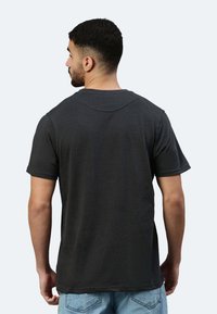 T-shirt nera a maniche corte con collo a giro, realizzata in morbido cotone. La vista posteriore mostra un design semplice con una vestibilità comoda e un orlo dritto.