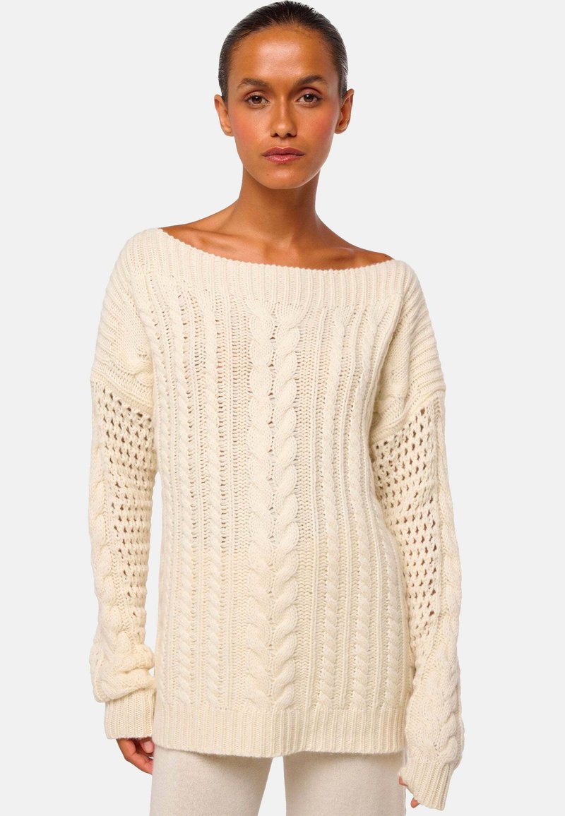 Cremfarbener Strickpullover mit weitem Halsausschnitt, strukturiertem Zopfmuster und offenknotigen Ärmeln. Weicher, dicker Stoff und gerippte Bündchen.