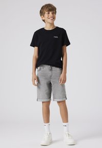 T-shirt en coton noir avec logo blanc, associé à un short en denim gris retroussé au bas, et des baskets blanches à semelles épaisses.