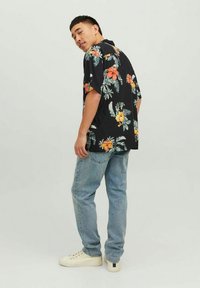 Camicia nera a maniche corte con un vivace motivo floreale in arancione e verde. Abbinata a jeans in denim blu chiaro e sneakers bianche.