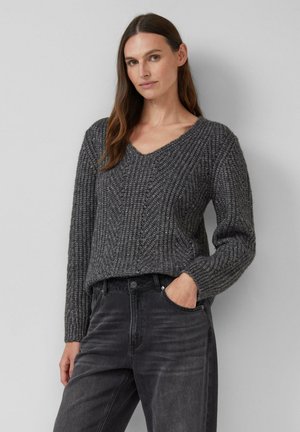 Grau gestrickter Pullover mit V-Ausschnitt, strukturiertem Muster und langen Ärmeln, kombiniert mit dunkelgrauen Jeans, die eine entspannte Passform zeigen.
