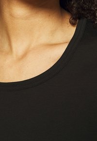 Černá bavlněná košile s širokým zaobleným výstřihem a hladkým povrchem, viditelné švy podél límce.