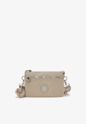 Beige crossbody bag with front zip pocket, adjustable strap, circular Kipling logo, and a small plush monkey keychain attached.