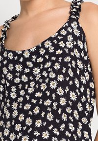 Black fabric top featuring a daisy floral print in white and yellow. Design includes ruffled straps and a wide neckline.