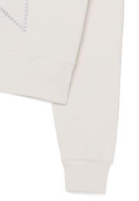 Cremefarbener Sweatshirt mit weicher Textur, das auf einer Seite ein erhabenes Muster aus kleinen hellgrauen Punkten und anpassungsfähige Bündchen aufweist.