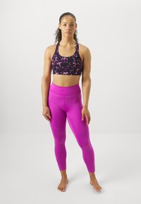 Reggiseno sportivo nero con motivo floreale rosa, abbinato a leggings rosa a vita alta. Tessuto morbido e design aderente.