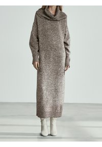 Robe pull en tricot à manches longues dans un motif texturé marron et crème, dotée d'un col bénitier et de poignets côtelés, assortie à des bottes crème.