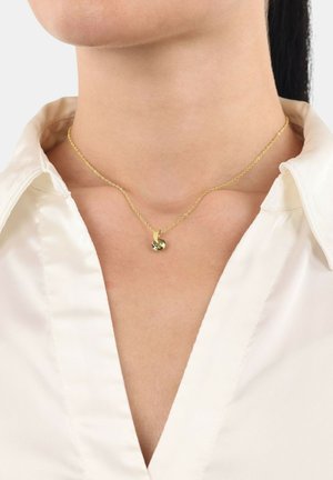 Collar de oro con un pequeño colgante de piedra preciosa verde, exhibido sobre una blusa blanca con escote en V. La cadena tiene un diseño delicado.