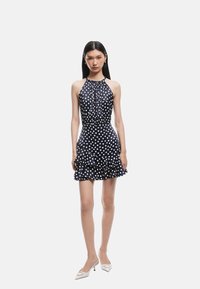 Vestido de lunares azul marino con cuello halter, con fruncido en la parte delantera y un dobladillo con volantes. Hecho de una tela suave, presenta una silueta ajustada.