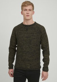 Mørkegrønn genser med rund hals laget av teksturert strikket stoff med svarte prikker, med lange ermer og en avslappet passform.