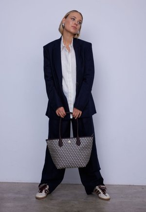 Woven handbag in neutral tones with a geometric pattern, featuring brown leather handles and accents. Rectangle shape with a flat base.
