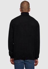 Svart genser med høy hals og lange ermer, ribbestrikket krage og hem. Kombinert med blå jeans som har jevn tekstur og slim fit-design.