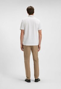 Vit kortärmad polo med krage, i kombination med ljusbeiga byxor. Skjortan har en subtil design längs kragen.