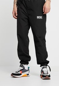 Black jogger pants with elastic waistband and logo detail. Paired with multi-colored sneakers featuring a mix of textures and colors.