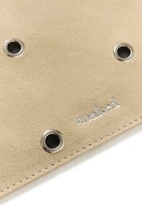 Tissu en suède beige avec trois œillets en métal et un bord surpiqué, présentant un logo embossé argenté discret "soaked".