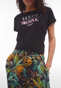 Camiseta negra de manga corta con el texto colorido "Hazlo realidad". Combinada con pantalones de corte holgado con un vibrante patrón de hojas tropicales.