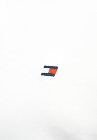 Λευκό βαμβακερό πουκάμισο με κεντημένο λογότυπο που περιλαμβάνει ένα ορθογώνιο σε κόκκινο, λευκό και ναυτικό μπλε. Απλή, ομαλή υφή.