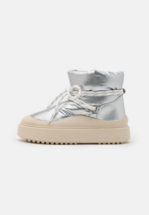 Silver metallic ankle boot with a padded upper, white laces, and a beige platform sole, featuring a textured rubber bottom for grip.