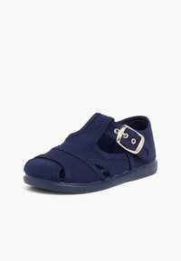 Navy blue fabric shoe with a closed toe, open sides, and a strap featuring a silver buckle. Soft texture and flat rubber sole.