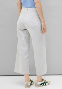 Gestreifte weite Hosen aus leichtem Stoff mit hoher Taille, zwei Gesäßtaschen und kombiniert mit beige-grünen Sneakers.