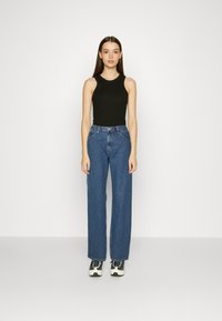 Top preto sem mangas com decote redondo, combinado com jeans azuis de cintura alta e pernas largas, e sapatilhas pretas e brancas.