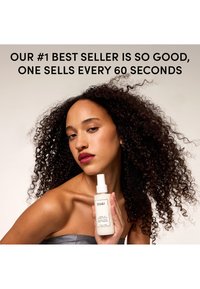Femme aux cheveux bouclés tenant une bouteille de OUAI Leave-In Conditioner, le texte ci-dessus indique qu'elle se vend toutes les 60 secondes comme un best-seller.