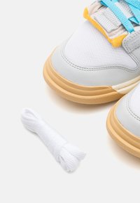 Scarpe da ginnastica grigio chiaro con mesh e pelle, dotate di suole in gomma beige e lacci blu, accompagnate da un ulteriore laccio bianco.