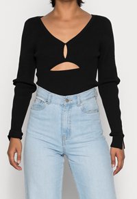 Haut noir à manches longues côtelé avec un décolleté en V profond et des découpes. Assorti à un jean taille haute bleu clair.