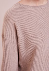 Pull en maille côtelée rose clair avec une coupe décontractée ; il présente un col rond et une texture horizontale subtile. Matière douce et confortable.