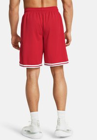 Pantalones cortos deportivos rojos con textura de malla, rayas blancas en los laterales y cinturilla elástica. Combinados con calcetines blancos y calzado.