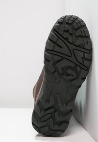 Czarna gumowa podeszwa z głębokim bieżnikiem dla lepszej przyczepności, brązowa cholewka z teksturowanym detalem, zaprojektowana do użytku na świeżym powietrzu.