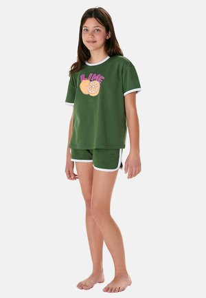 Fille debout pieds nus portant un t-shirt vert avec l'inscription "LIME" et un dessin de fruit, assorti à un short vert avec un bord blanc.