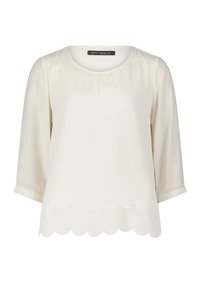 Blouse de couleur crème avec manches trois-quarts et détail d'ourlet festonné, présentant un col rond et une texture de tissu douce.