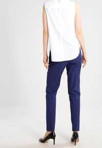 Vit ärmlös topp med slits på ryggen, kombinerad med marinblå mönstrade byxor och svarta högklackade skor. Fokusera på rena linjer och skräddarsydd passform.