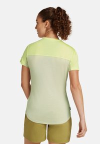 Camisa de manga corta verde claro con un panel trasero transparente y textura acanalada. Con dobladillo redondeado y un diseño sencillo, combinada con pantalones cortos verde oliva.