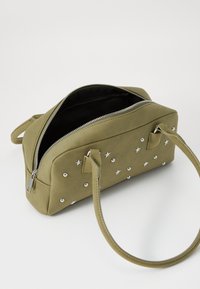 Sac à main vert olive avec des embellissements en étoile argentés, fermeture éclair, poignées doubles et doublure intérieure noire. Design élégant et structuré.