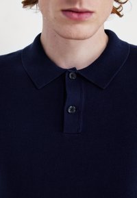 Granatowa koszulka polo wykonana z dzianiny, z kołnierzykiem i dwoma guzikami oraz drobnymi prążkowanymi detalami.