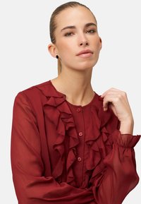 Rode blouse met ruches, lange mouwen, knoopsluiting aan de voorkant en doorschijnende stof. Geaccentueerde manchetten en gelaagde ruches zorgen voor structuur en detail.