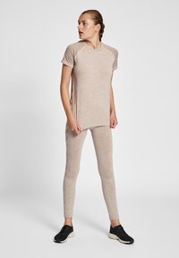 Jasnobeżowa sportowa bluzka z teksturowanymi krótkimi rękawami w połączeniu z pasującymi legginsami. Całość charakteryzuje się dopasowanym krojem i gładkim materiałem.