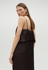 Tmavohnedé plisované šaty s ramienkami spaghetti. Na vrchu s vrstveným dizajnom, hladká textúra a jemný lesk. Minimalistické a elegantné.