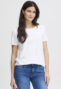 Balti trumpomis rankovėmis medvilninė marškinėliai su apvalia iškirpte ir laisvo silueto, derinami su mėlynais džinsais iš džinsinio audinio.