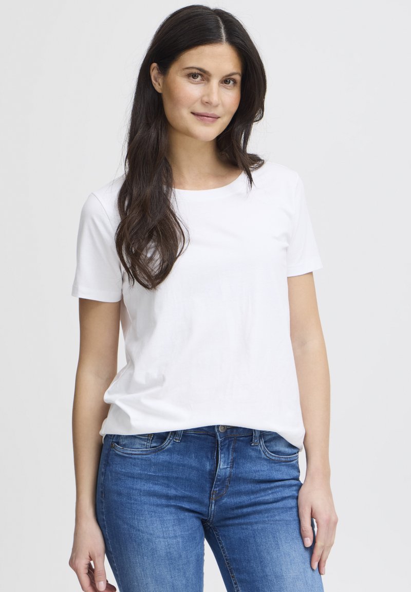 Balti trumpomis rankovėmis medvilninė marškinėliai su apvalia iškirpte ir laisvo silueto, derinami su mėlynais džinsais iš džinsinio audinio.