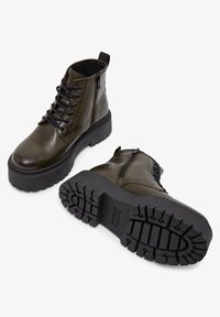 Bottines à cheville en cuir vert olive avec des lacets noirs, fermeture éclair sur le côté, semelle en caoutchouc épaisse et semelle texturée pour une meilleure adhérence.