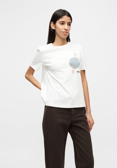 Λευκό βαμβακερό μπλουζάκι με κοντά μανίκια, με στρογγυλό μπλε γραφικό και καφέ ρίγες στο μπροστινό μέρος, συνδυασμένο με σκούρο καφέ παντελόνι.