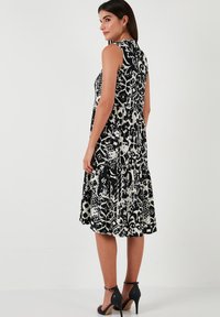 Black and white floral-patterned sleeveless dress with tiered ruffles, featuring a high neckline and a flowy silhouette.