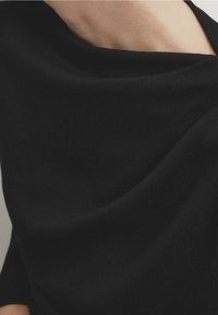 Black draped top in a smooth fabric, featuring soft texture and a wide neckline; cut details create gentle folds in the material.