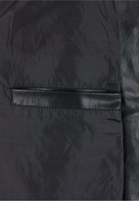 Schwarze Pufferjacke mit einem strukturierten Lederakzent. Verfügt über eine flache Tasche und eine glatte, glänzende Oberfläche des Stoffes.
