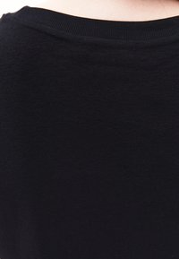 Černý pletený kousek s jemnou strukturou, s kulatým výstřihem a decentním švem na zadní straně. Žádné další vzory ani akcenty.