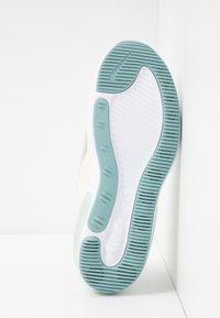 Sula av en vit Nike Air Max-sko med ljusblå gummi-sula och präglad Nike-logotyp, vinklad mot en vit bakgrund.